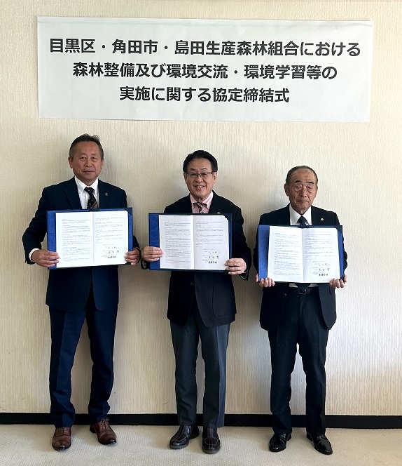 署名者3名が協定書を掲げている写真。