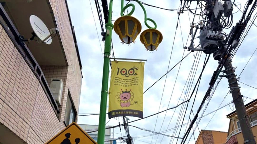 油面小学校開校100周年記念キャラクター「百周の王アブライオン」が描かれた、100周年記念フラッグが青空になびいています。