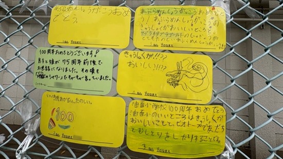 「あぶらめん住区 街かど美術展」のフェンス展示のアップ写真。「給食がおいしい」などのメッセージが並ぶ。