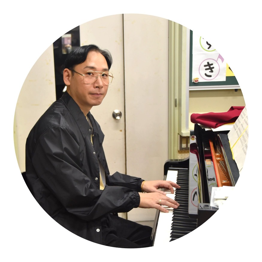 クラムボン ミトさんの写真。油面小学校の音楽室でピアノの前に座っている。