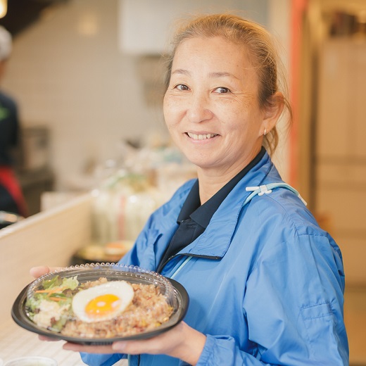 株式会社オクヨシの代表を務める芹田明美さんの写真。お弁当を持っています。